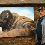 Duane Hada applies final strokes to a bison painting on an Artefex all-in-panel mounted against a rustic stone wall