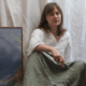 Artist Kaysha Siemens holds paintbrushes while seated beside an Artefex Tempanel-mounted cloud painting in her studio